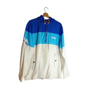 May include: A vintage blue, turquoise, and white hooded jacket with a half-zip closure. The jacket features a color-block design and a small logo on the sleeve. The jacket has two front pockets with button closures.