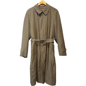 Könnte beinhalten: Ein beigefarbener Trenchcoat mit Gürtel und Knopfverschluss, hängt an einem Holzbügel. Der Mantel hat ein klassisches Design mit Kragen und langen Ärmeln. Der Mantel ist aus strapazierfähigem Stoff gefertigt.