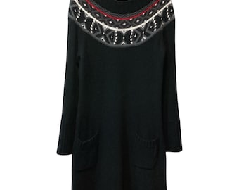Könnte beinhalten: Schwarzes Strickkleid mit gemustertem Einsatz. Der Einsatz hat ein geometrisches Design in Rot, Weiß und Grau. Das Kleid hat lange Ärmel und zwei Vordertaschen. Das Kleid hängt an einem Holzbügel.