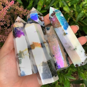 Pode incluir: Cinco pontas de cristal branco iridescente com um brilho arco-íris. As pontas estão dispostas em um cacho e têm uma textura natural e áspera.