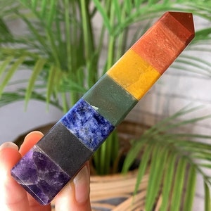 Op de afbeelding: Een zeven-chakra kristallen staf met een puntige punt. De staf is gemaakt van zeven verschillende gekleurde stenen, die elk een ander chakra vertegenwoordigen. De stenen zijn gerangschikt in een regenboogpatroon, beginnend met amethist onderaan en eindigend met rode jaspis bovenaan.