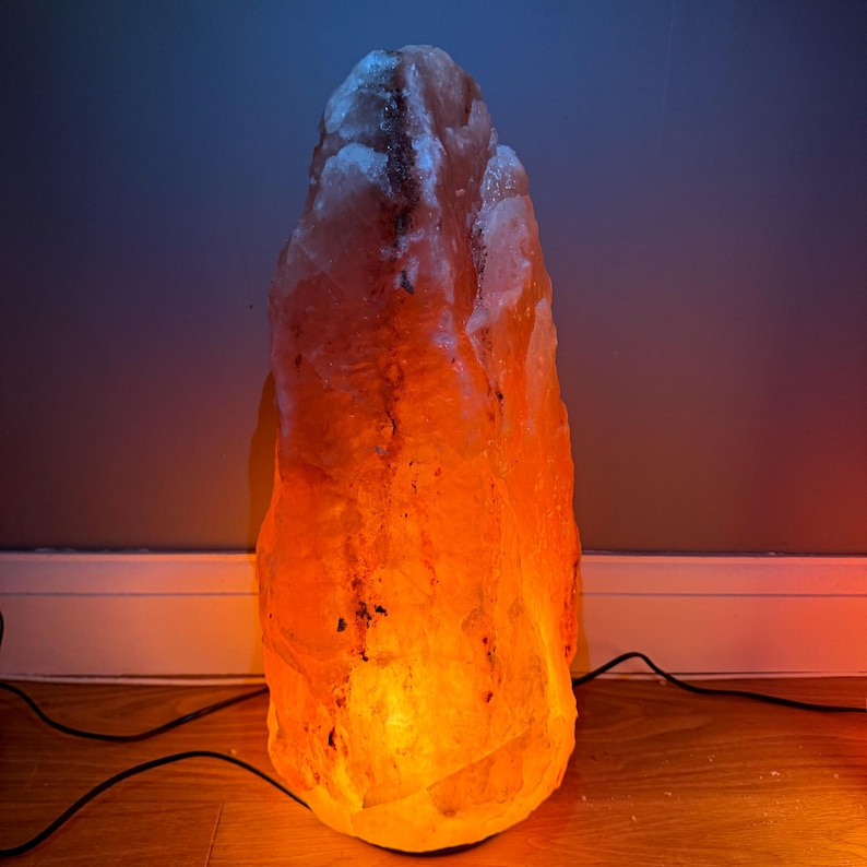 May include: A large, orange Himalayan salt lamp with a warm, orange glow. The lamp is shaped like a tall, pointed rock and is lit from within.