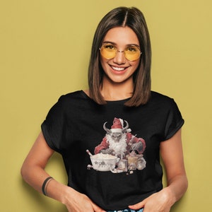 May include: A black t-shirt with a graphic of a demon dressed as Santa Claus baking cookies. The demon has horns, a beard, and a red hat. The graphic is in a cartoon style.