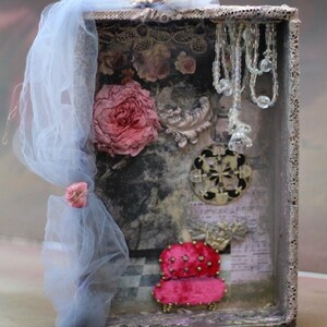 May include: A vintage-style shadow box with a pink rose, a pink velvet armchair, and a beaded chandelier. The box is decorated with lace, paper, and other embellishments.