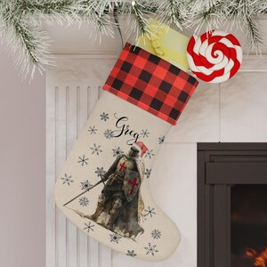 May include: A Christmas stocking with a red and black buffalo plaid cuff. The stocking features a watercolor image of a knight, the name "Greg", and snowflake accents. A red and white swirled lollipop is attached.