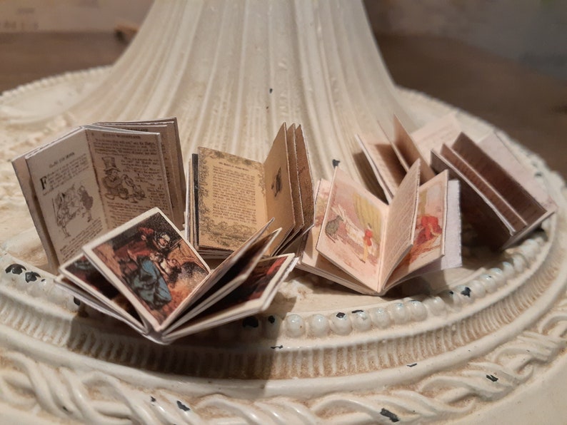 May include: A collection of miniature open books with detailed illustrations and text. The pages are aged with a vintage aesthetic, and the covers feature colorful images. The books are arranged on a decorative, off-white surface.