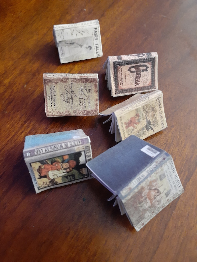 May include: A collection of miniature books with visible titles like "Fairy Tales," "Cinderella," and "Snow White." The books have aged, vintage-style covers with illustrations and text. The books are arranged on a wooden surface.