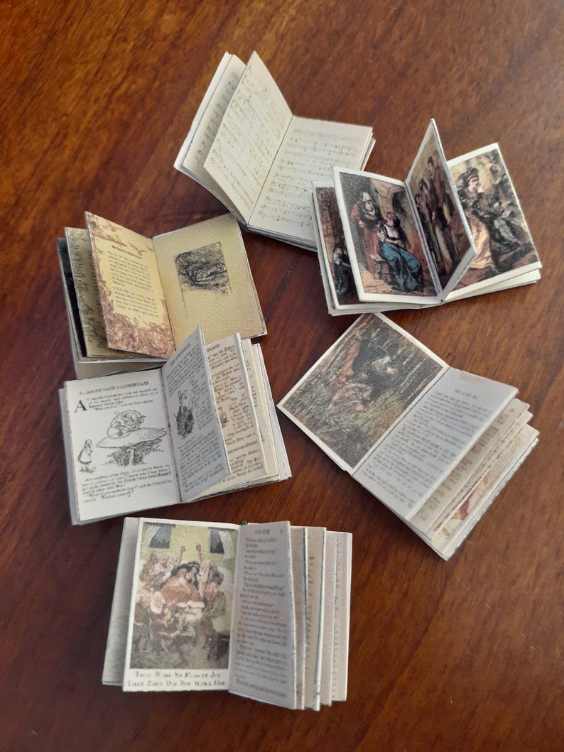 May include: A collection of miniature open books with detailed illustrations and text. The pages display various images and handwritten notes, suggesting a vintage or antique aesthetic. The books are arranged on a wooden surface.