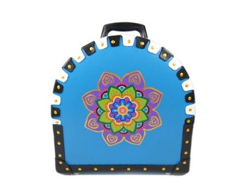 May include: A blue, round, hard-sided suitcase with a black handle and gold studs. The suitcase is decorated with a colorful mandala design.