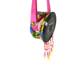 May include: A black vinyl record shaped crossbody bag with a pink strap and colorful print. The bag has pink and yellow tassels hanging from the bottom.