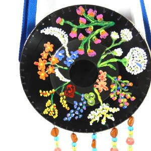 May include: A black vinyl record painted with a colorful floral design. The record is hanging from a blue ribbon and has colorful beads hanging from the bottom.