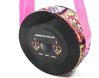 May include: A black vinyl record with a colorful fabric cover and pink straps. The record has a label that says "Summer of Love Art" with peace signs and the words "Peace, Love, Music".