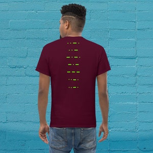 Pode incluir: Uma camiseta vinho com um design gráfico verde nas costas. O design é uma série de traços e pontos.