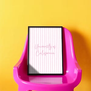 May include: A framed print with the text "University of California" in a pink script font. The print has a pink and white striped background and is set in a black frame. The frame rests on a bright pink chair against a yellow background.