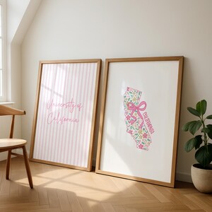May include: Two framed art prints. One features pink and white vertical stripes with the text "University of California" in pink script. The other print displays a floral California map with a pink bow and the word "California".
