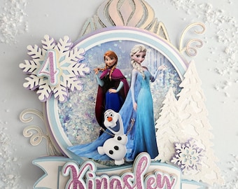 Può includere: Un topper per torta a tema Frozen con Elsa e Anna del film Disney Frozen. Il topper include un fiocco di neve, uno stendardo bianco e blu con il nome Kingsley e una corona bianca e blu. Il topper è perfetto per una festa di compleanno a tema Frozen.