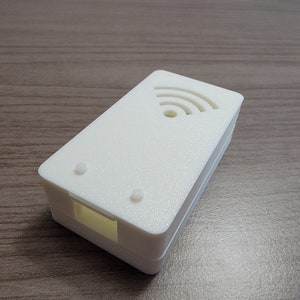 May include: A white plastic enclosure with a cutout for a WiFi symbol. The enclosure has two small holes on the top and a rectangular opening on the side.