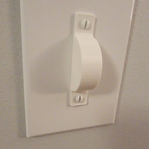 May include: White plastic light switch cover with a rounded handle. The switch cover is mounted on a wall.
