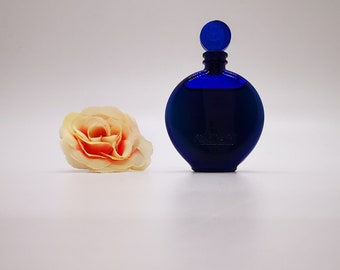 May include: A blue glass bottle of perfume with a round, flat bottom and a blue cap. The bottle is sitting on a white surface.