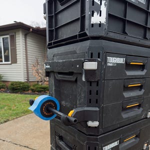May include: A stack of black Toughbuilt Stacktech toolboxes with yellow accents. The top toolbox has a blue tape wrapped around the handle. The toolboxes are on wheels and have a handle for moving them.