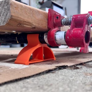 Può includere: Supporti in plastica arancione per un morsetto per tubi rosso. Il morsetto tiene in posizione una tavola di legno.