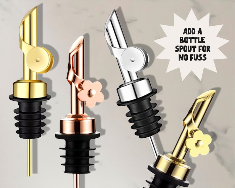 May include: Four metal bottle spouts in gold, copper, and silver tones. Each spout has a black rubber stopper. One gold spout has a flower accent. Text reads: ADD A BOTTLE SPOUT FOR NO FUSS.