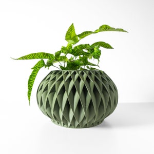 May include: A green, geometric planter with a leafy green plant inside. The planter has a unique, textured design with a rounded shape.