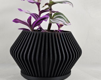 May include: A black, geometric planter with a ribbed design holds a purple and green houseplant.