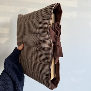 Op de afbeelding: Een bruin en tan geruite boekomslag met een donkerbruine striksluiting. De omslag is gewatteerd en heeft een zachte, gewatteerde textuur. De boekomslag is ontworpen om het uiterlijk van een boek te beschermen en te verbeteren.