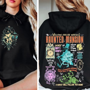 May include: Black hooded sweatshirt with a graphic print of the Haunted Mansion attraction from Disneyland. The print features the text "The Welcome Foolish Mortals Haunted Mansion" with a clock, ghosts, and the text "999 Happy Haunts".