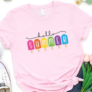 May include: Pink t-shirt with the text "hello summer" in black script with rainbow popsicle graphics.
