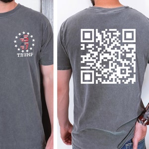 May include: A dark gray t-shirt with a white American flag design and the word "TRUMP" printed on the front. The back of the shirt features a white QR code.