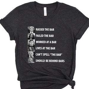 May include: A dark gray t-shirt with a white graphic print of a list of people and their relationship to the word "bar". The text reads: "Raised the bar, Failed the bar, Worked at a bar, Lives at the bar, Can't spell "the bar", Should be behind bars."