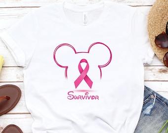 Könnte beinhalten: Weißes T-Shirt mit einem rosa Band und Mickey-Maus-Ohren und dem Wort "SURVIVOR" darunter.