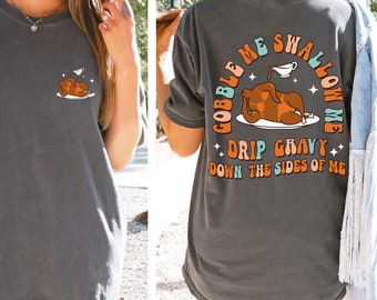 May include: A gray t-shirt with a Thanksgiving-themed graphic on the back. The graphic features a cartoon turkey with the text "Gobble Me Swallow Me Drip Gravy Down The Sides Of Me".