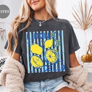 May include: Dark gray t-shirt with a lemon-themed graphic. The design features yellow lemons, blue stripes, and the words "LIMONCELLO" in blue. The shirt is a casual, comfortable style.
