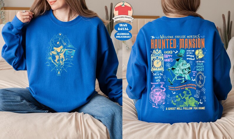 May include: A blue sweatshirt with a graphic print of the Haunted Mansion attraction from Disneyland. The print features the text "Welcome Foolish Mortals Haunted Mansion" and various characters from the attraction, including the Ghost Host.