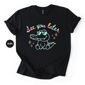 Puede incluir: Camiseta negra con un dise&ntilde;o de un cocodrilo con gafas de sol y la frase "See you later" en colores pastel. El dise&ntilde;o incluye estrellas. Tambi&eacute;n se ve un c&iacute;rculo negro con la palabra "Black".