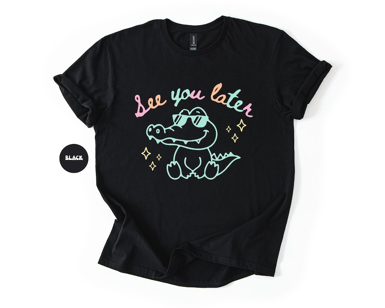 Puede incluir: Camiseta negra con un dise&ntilde;o de un cocodrilo con gafas de sol y la frase "See you later" en colores pastel. El dise&ntilde;o incluye estrellas. Tambi&eacute;n se ve un c&iacute;rculo negro con la palabra "Black".