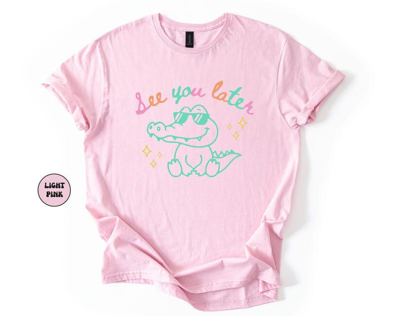 Puede incluir: Camiseta rosa claro con un cocodrilo de dibujos animados con gafas de sol. El texto "See you later" est&aacute; escrito encima del cocodrilo en colores pastel. La camiseta tiene mangas enrolladas y cuello redondo.