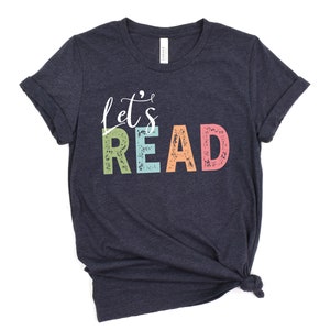 May include: A dark blue t-shirt with the text "Let's Read" in colorful letters. The letters are in a retro style with a distressed look.