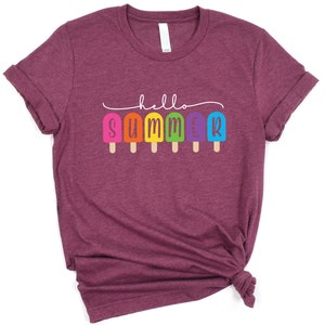May include: A maroon t-shirt with the text "hello summer" in white lettering. The text is surrounded by a line of rainbow popsicles.