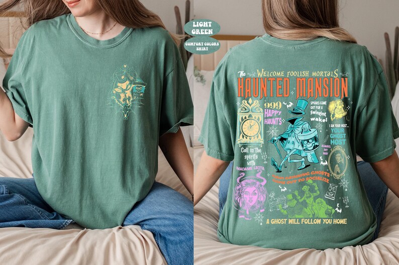 May include: A light green t-shirt with a graphic print of the Haunted Mansion attraction from Disneyland. The text on the shirt reads "The Welcome Foolish Mortals Haunted Mansion 999 Happy Haunts".