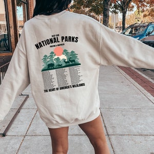 May include: A beige sweatshirt with a graphic print on the back that says "Keep Our National Parks Pristine & Unspoiled" with a green forest scene and the text "The Heart of America's Wildlands".
