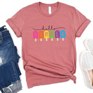 May include: A dusty rose t-shirt with the text "hello summer" in black lettering. The text is decorated with a row of colorful popsicles.