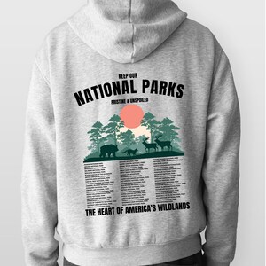 May include: Gray hooded sweatshirt with a graphic print of a forest scene and the text "Keep Our National Parks Pristine & Unspoiled". The graphic also includes a list of national parks in the United States. The text "The Heart of America's Wildlands" is printed below the list.