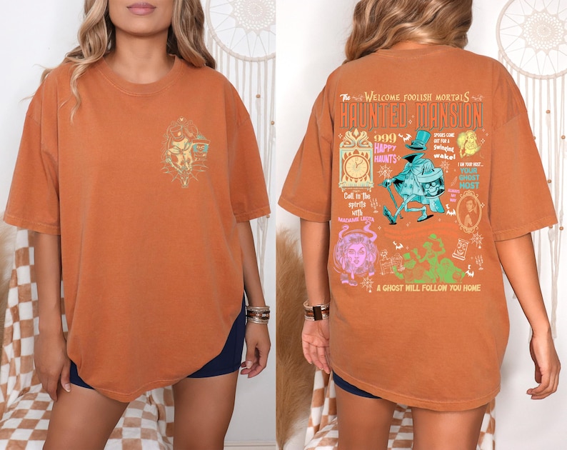 May include: A burnt orange t-shirt with a graphic print of a haunted mansion. The text on the shirt reads "The Welcome Foolish Mortals Haunted Mansion 666 Happy Haunts Call in the spirits with a midnight light A ghost will follow you home."