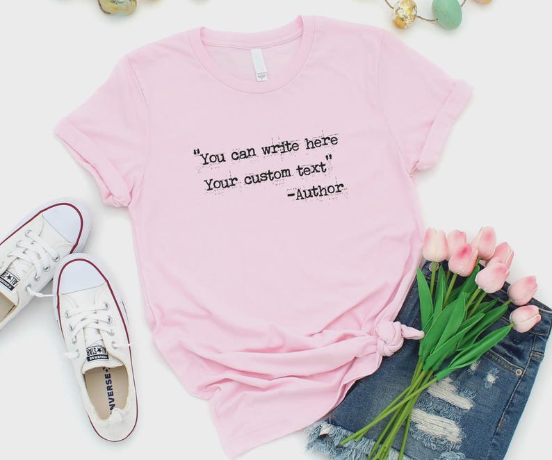 Może przedstawiać: Jasnor&oacute;żowa koszulka z czarnym napisem "You can write here Your custom text". Koszulka jest zawiązana na dole i połączona z dżinsowymi szortami, białymi trampkami i r&oacute;żowymi tulipanami.