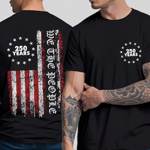 Może przedstawiać: Czarna koszulka z postarzanym wzorem amerykańskiej flagi na plecach z napisem "We the People" i "250 Years". Prz&oacute;d koszulki ma mniejszy wz&oacute;r "250 Years". Okrągły dekolt.