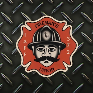 以下が含まれることがあります： ヘルメットと口ひげをつけた漫画の消防士が描かれた、赤と白の消防士組合のステッカー。ステッカーには「Fireman's Union」と「IAFF 372」の文字が書かれています。